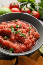 Photo of Delicious spicy salsa sauce in bowl and nacho chips on table, closeup