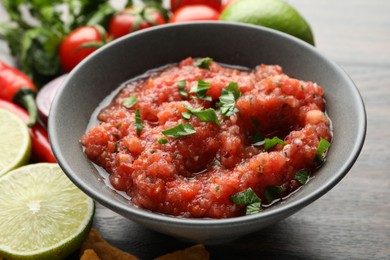 Photo of Delicious spicy salsa sauce in bowl and products on wooden table, closeup