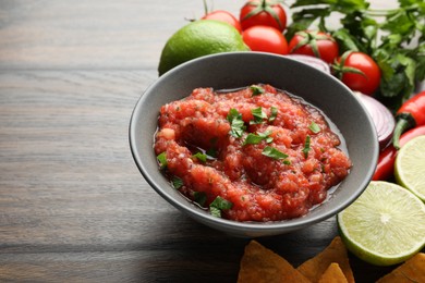 Delicious spicy salsa sauce in bowl and products on wooden table, closeup. Space for text