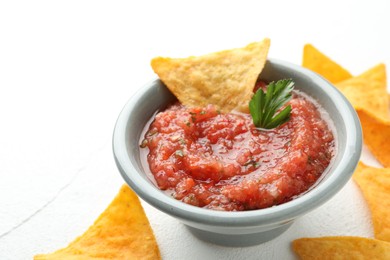 Delicious spicy salsa sauce in bowl and nacho chips on white table, closeup