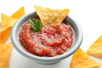 Photo of Delicious spicy salsa sauce in bowl and nacho chips on white table, closeup