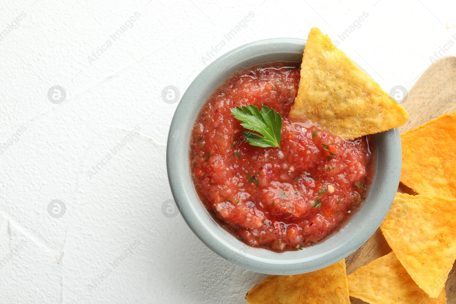 Photo of Delicious spicy salsa sauce in bowl and nacho chips on white textured table, flat lay. Space for text