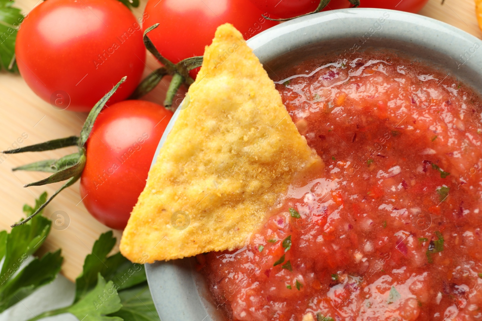 Photo of Delicious spicy salsa sauce with nacho chip in bowl and ingredients on wooden table, flat lay