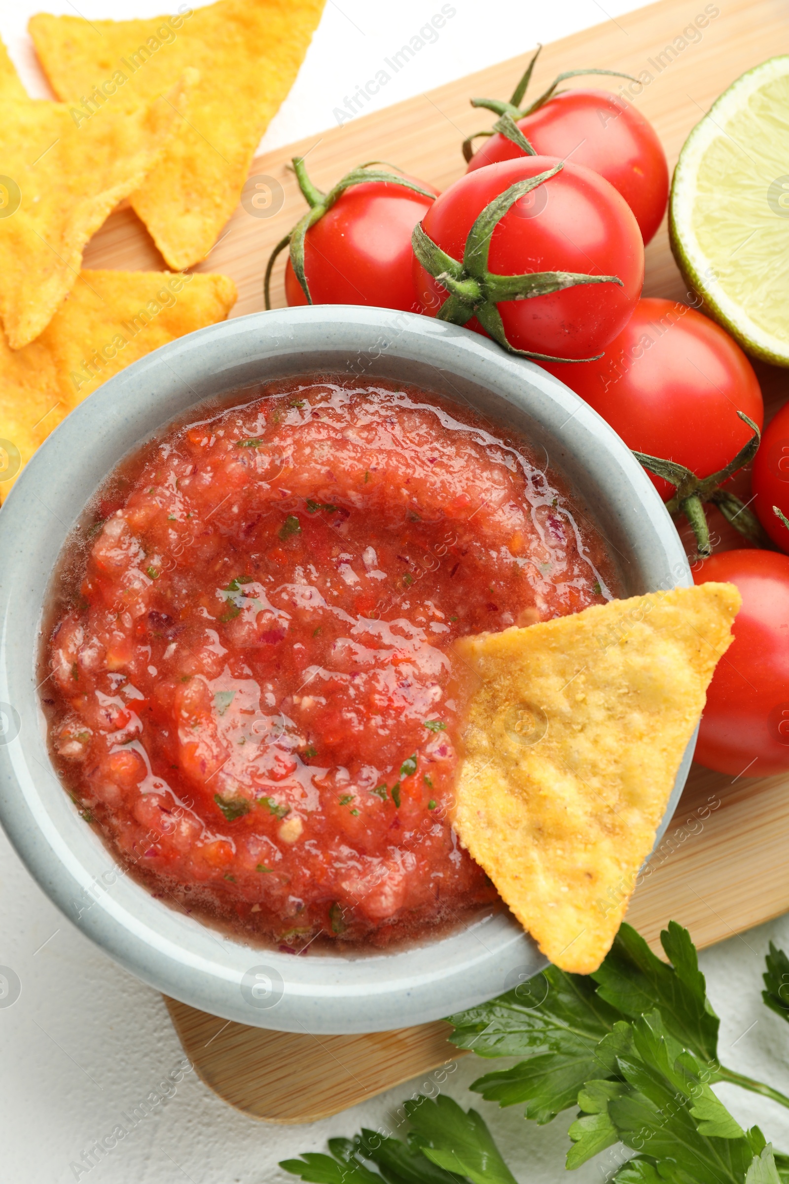 Photo of Delicious spicy salsa sauce with nacho chip in bowl and ingredients on white textured table, flat lay