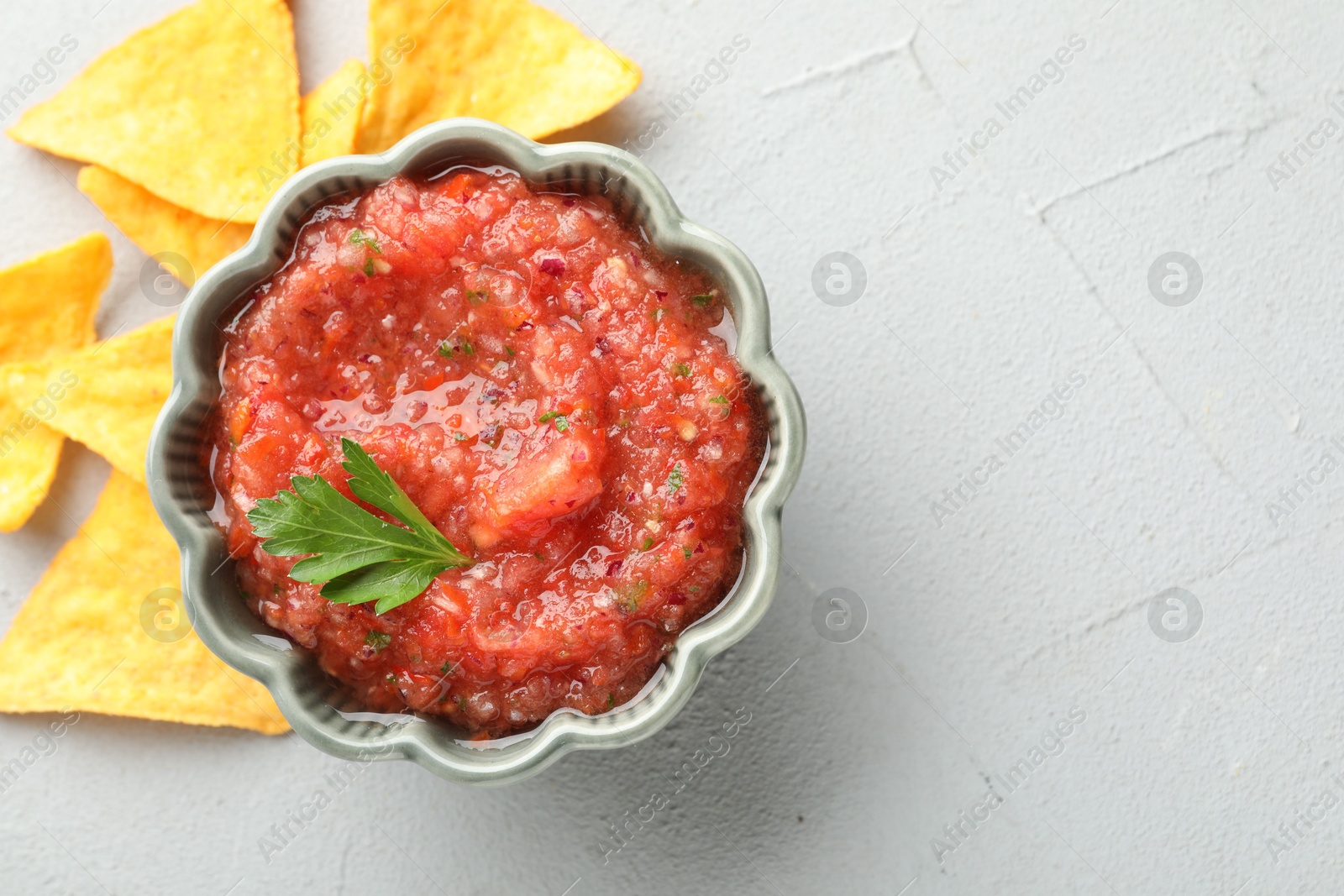 Photo of Delicious spicy salsa sauce in bowl and nacho chips on grey textured table, flat lay. Space for text