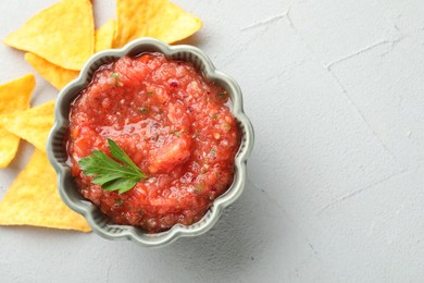 Delicious spicy salsa sauce in bowl and nacho chips on grey textured table, flat lay. Space for text