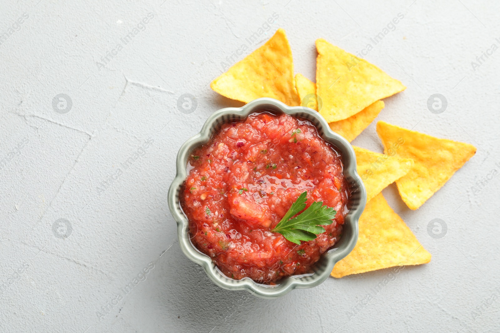 Photo of Delicious spicy salsa sauce in bowl and nacho chips on grey textured table, flat lay. Space for text