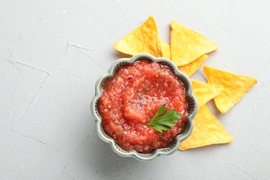 Photo of Delicious spicy salsa sauce in bowl and nacho chips on grey textured table, flat lay. Space for text