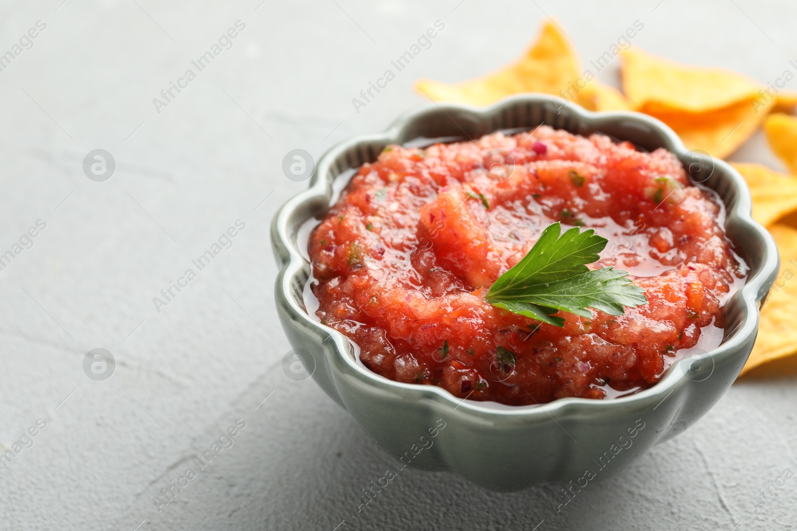 Photo of Delicious spicy salsa sauce in bowl on grey textured table, closeup. Space for text