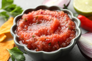 Photo of Delicious spicy salsa sauce in bowl and products on grey textured table, closeup