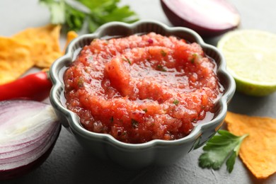 Delicious spicy salsa sauce in bowl and products on grey textured table, closeup