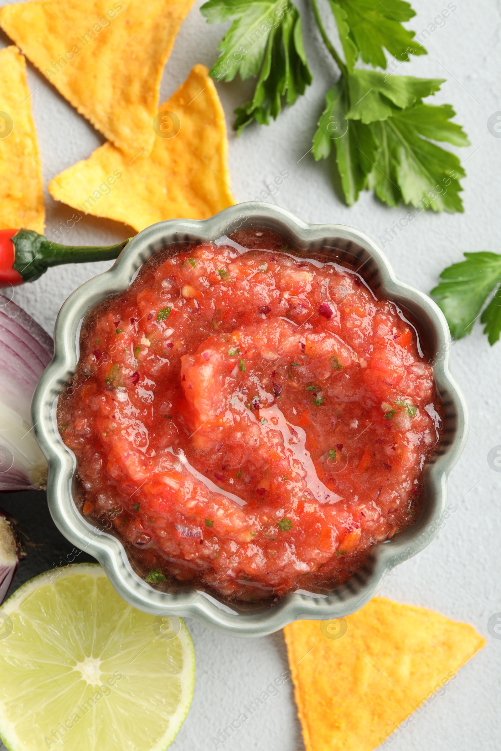 Photo of Delicious spicy salsa sauce in bowl and products on grey textured table, flat lay