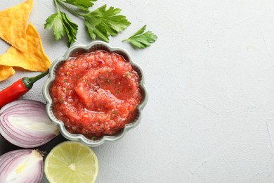 Delicious spicy salsa sauce in bowl and products on grey textured table, flat lay. Space for text