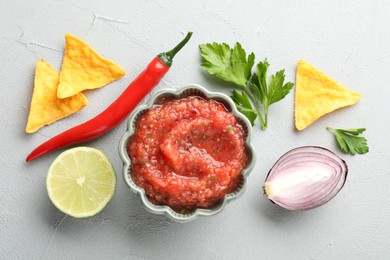 Photo of Delicious spicy salsa sauce in bowl and products on grey textured table, flat lay