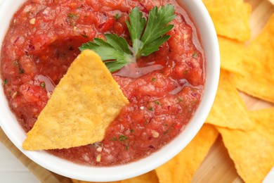 Photo of Delicious spicy salsa sauce with nacho chip in bowl on white table, top view