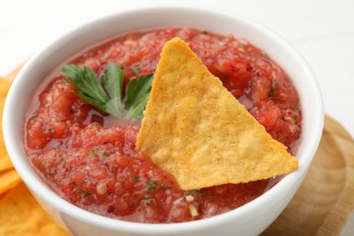 Photo of Delicious spicy salsa sauce with nacho chip in bowl on white table, closeup