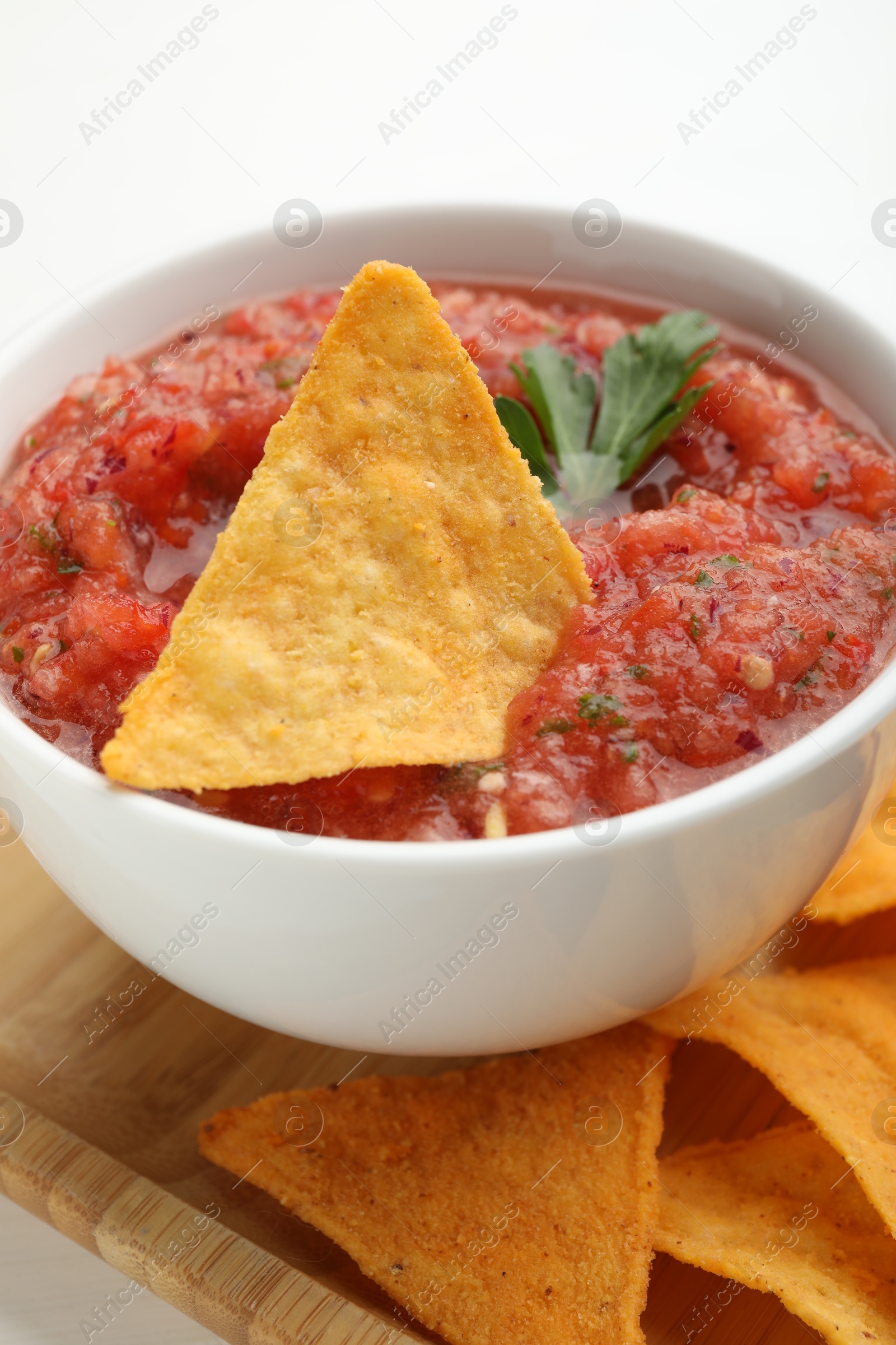 Photo of Delicious spicy salsa sauce with nacho chip in bowl on white table, closeup