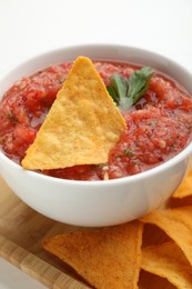 Delicious spicy salsa sauce with nacho chip in bowl on white table, closeup