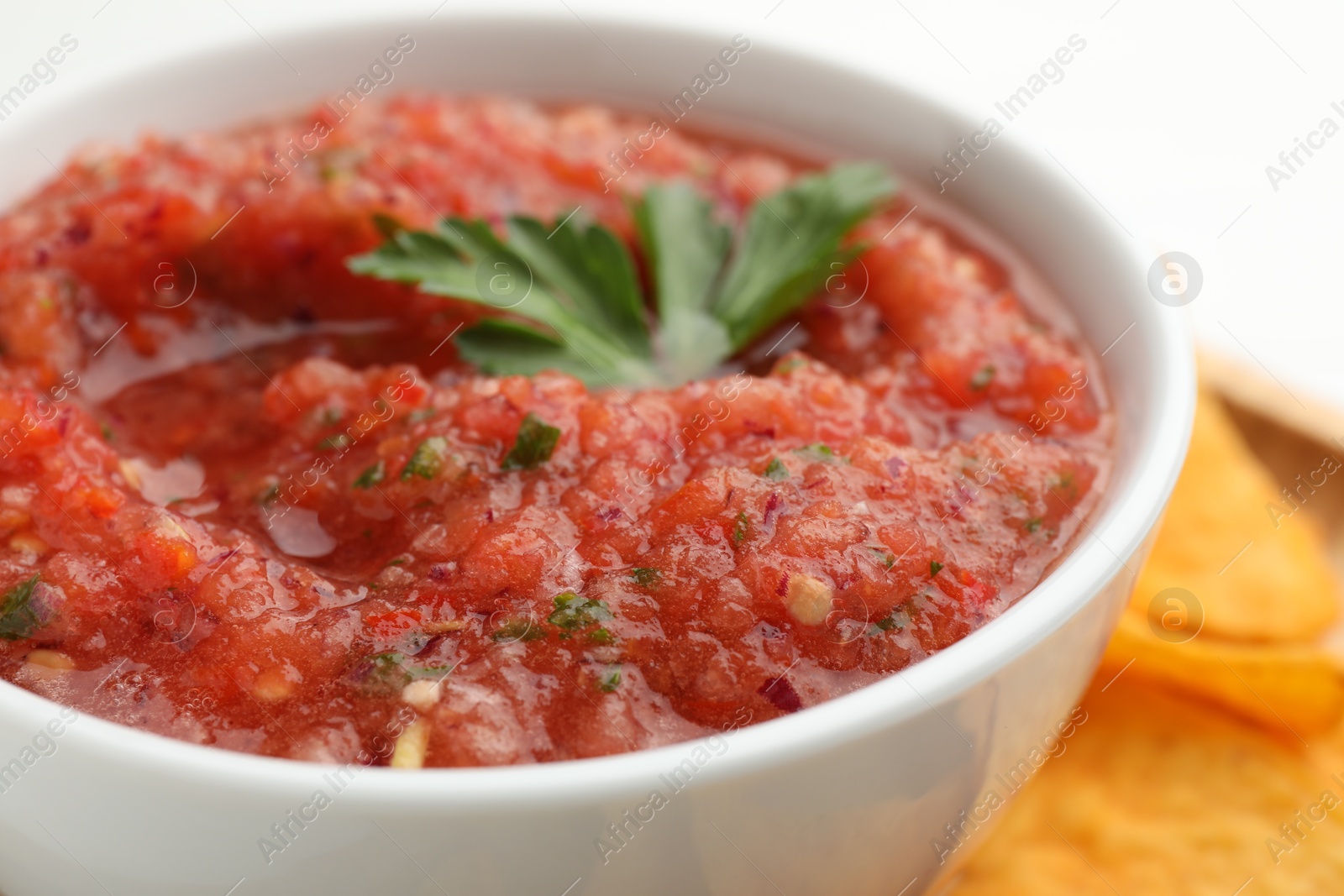 Photo of Delicious spicy salsa sauce with nacho chip in bowl on blurred background, closeup