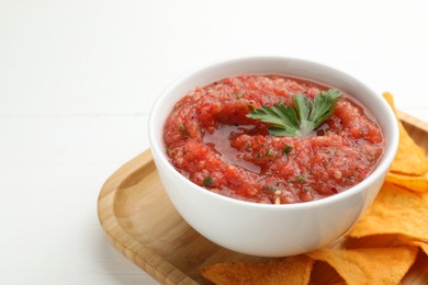 Delicious spicy salsa sauce in bowl and nacho chips on white wooden table, closeup