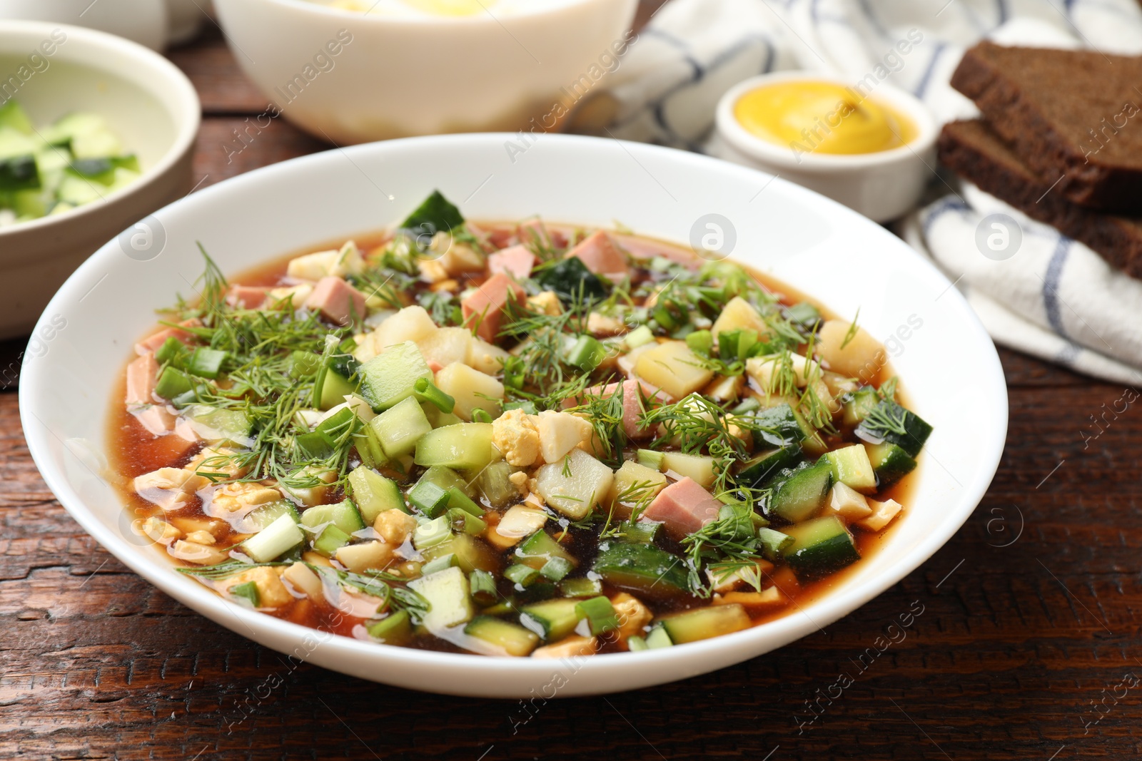 Photo of Tasty okroshka soup with kvass and ingredients on wooden table, closeup