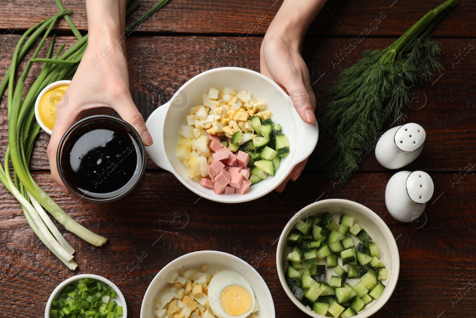 Photo of Making okroshka soup. Woman with bowl and different ingredients at wooden table, top view