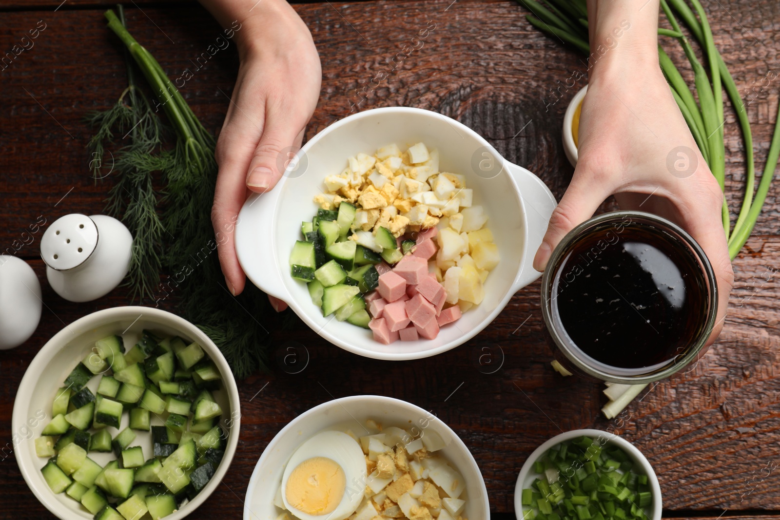 Photo of Making okroshka soup. Woman with bowl and different ingredients at wooden table, top view