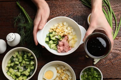 Photo of Making okroshka soup. Woman with bowl and different ingredients at wooden table, top view