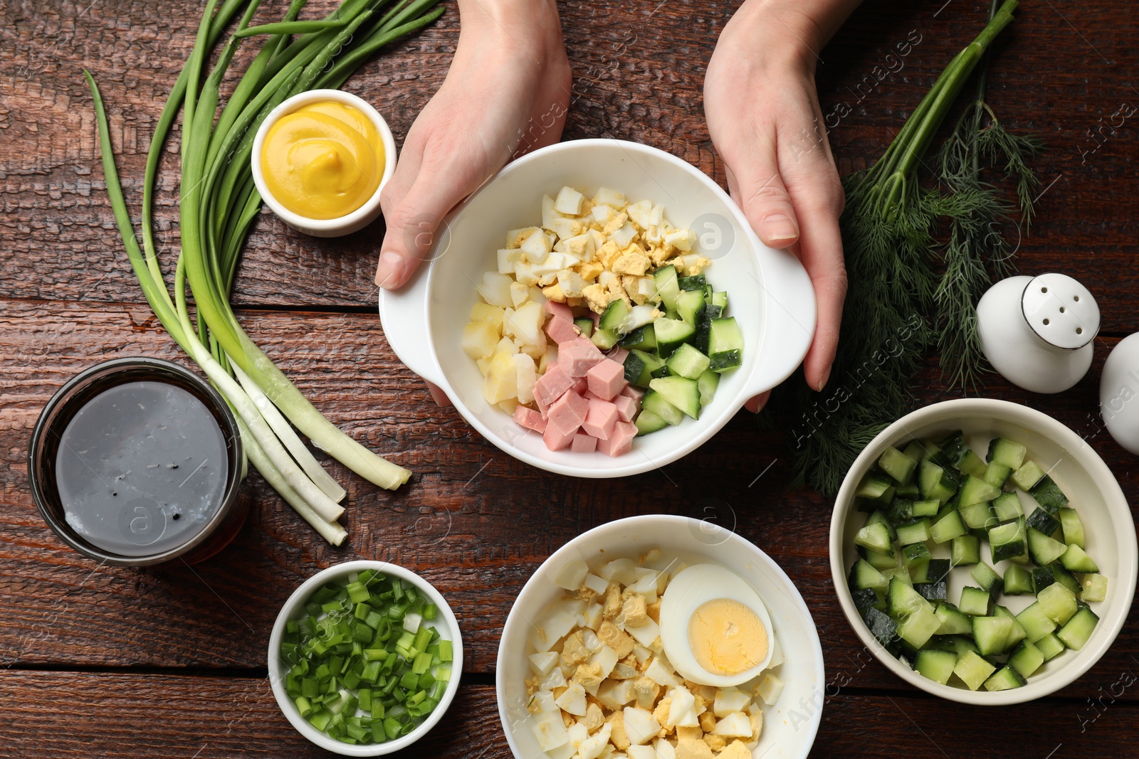 Photo of Making okroshka soup. Woman with bowl and different ingredients at wooden table, top view