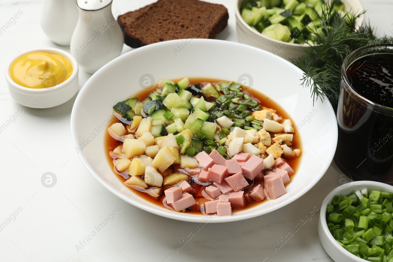 Photo of Tasty okroshka soup with kvass and ingredients on white marble table, closeup