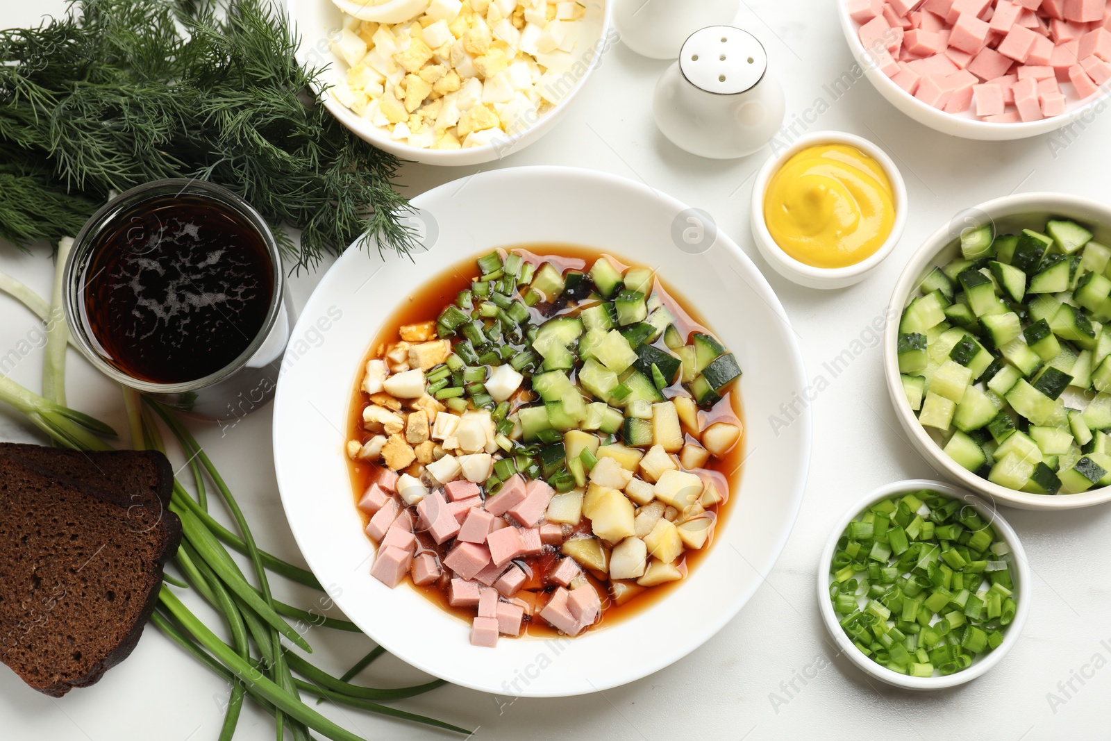 Photo of Tasty okroshka soup with kvass and ingredients on white marble table, flat lay