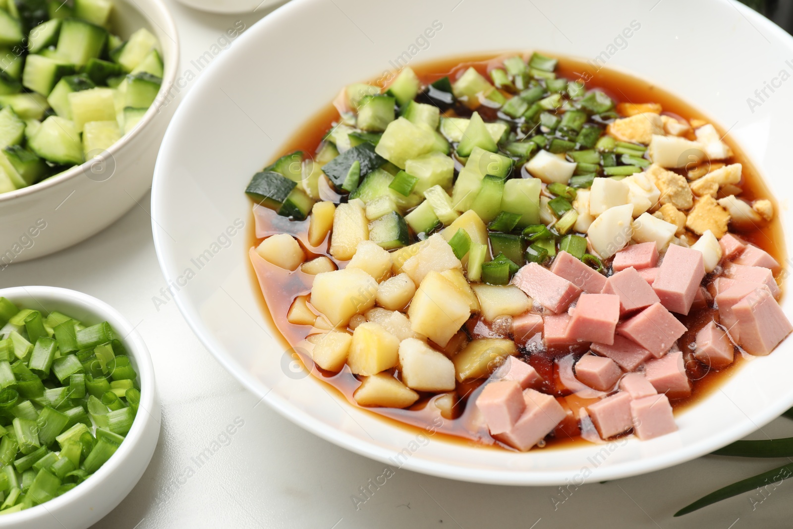 Photo of Making okroshka soup. Different ingredients in bowl on white marble table, closeup