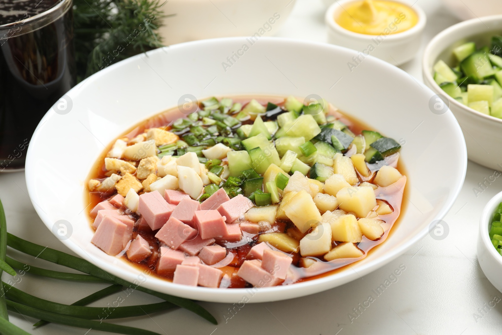 Photo of Making okroshka soup. Different ingredients in bowl on white marble table, closeup