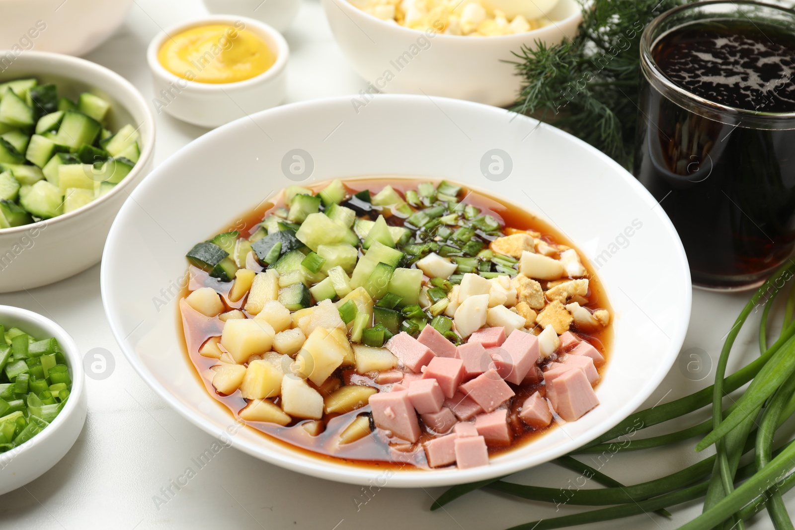 Photo of Making okroshka soup. Different ingredients in bowl on white marble table, closeup