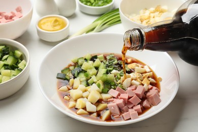 Making okroshka soup. Pouring kvass into bowl with different ingredients on white marble table, closeup