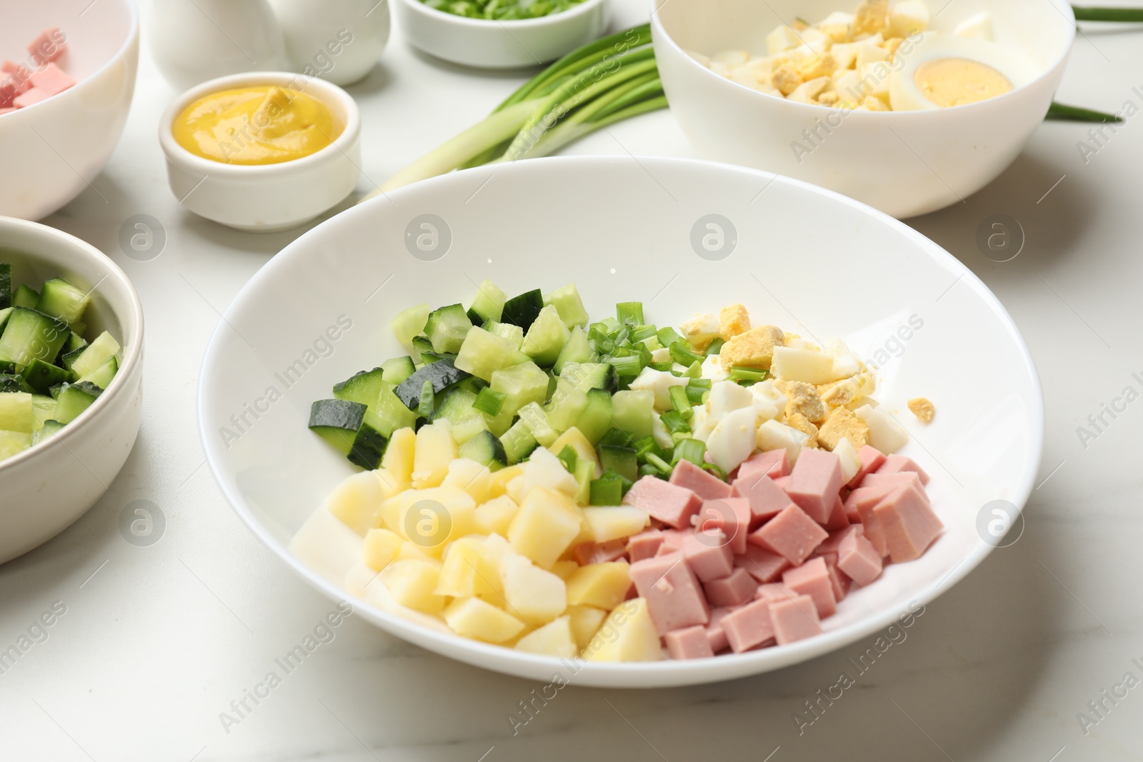 Photo of Making okroshka soup. Different ingredients in bowl on white marble table, closeup