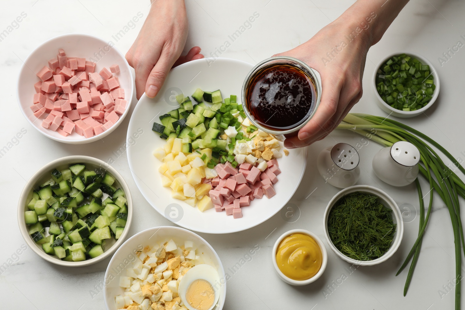 Photo of Making okroshka soup. Woman with bowl and different ingredients at white marble table, top view