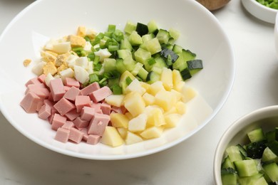 Photo of Making okroshka soup. Different ingredients in bowl on white marble table, closeup