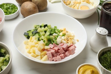 Photo of Making okroshka soup. Different ingredients in bowl on white marble table, closeup