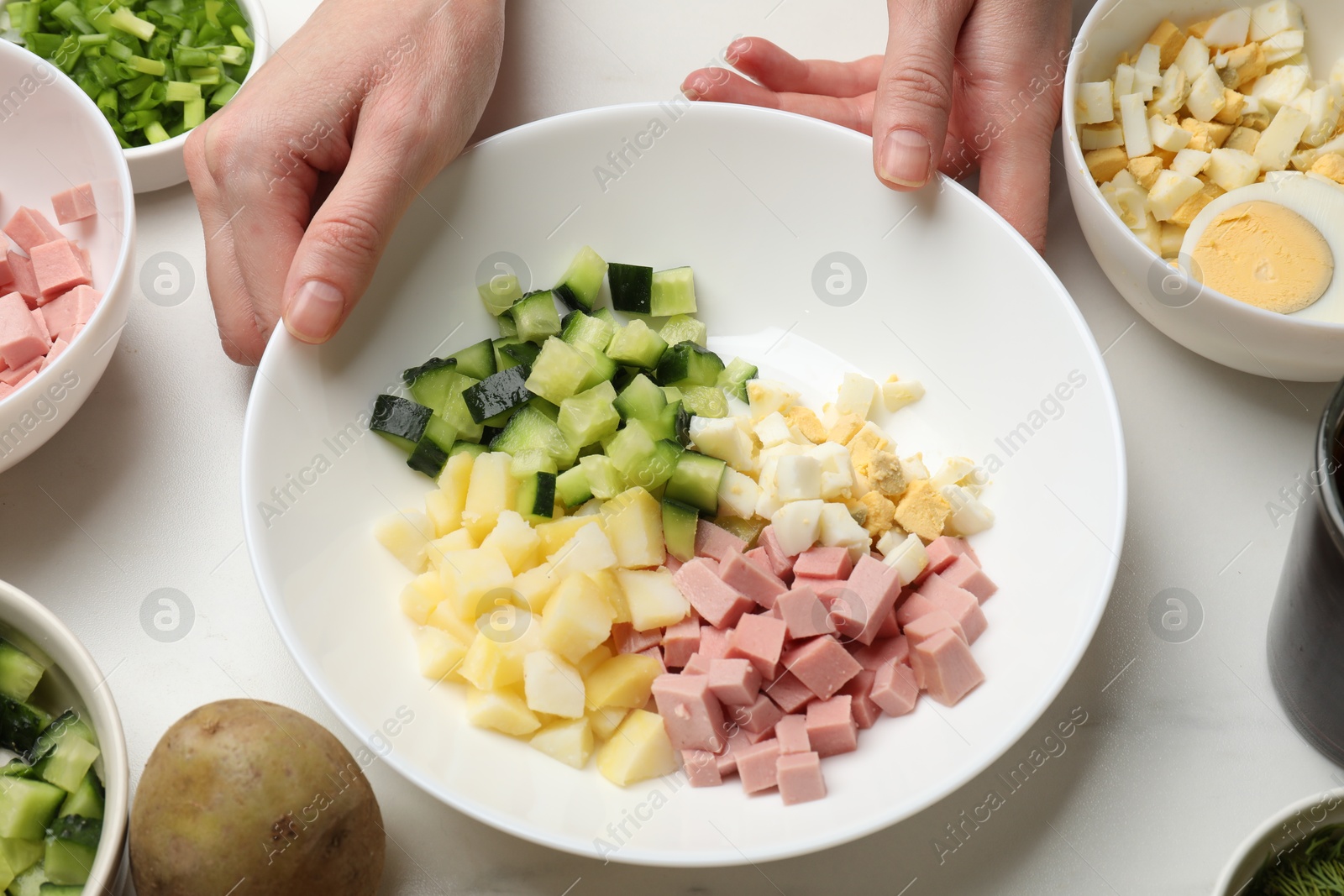 Photo of Making okroshka soup. Woman with bowl and different ingredients at white marble table, closeup