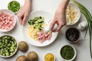 Photo of Making okroshka soup. Woman adding salt into bowl with different ingredients at white marble table, top view