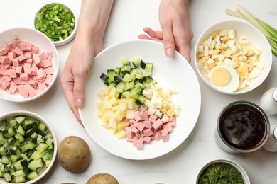 Photo of Making okroshka soup. Woman with bowl and different ingredients at white marble table, top view