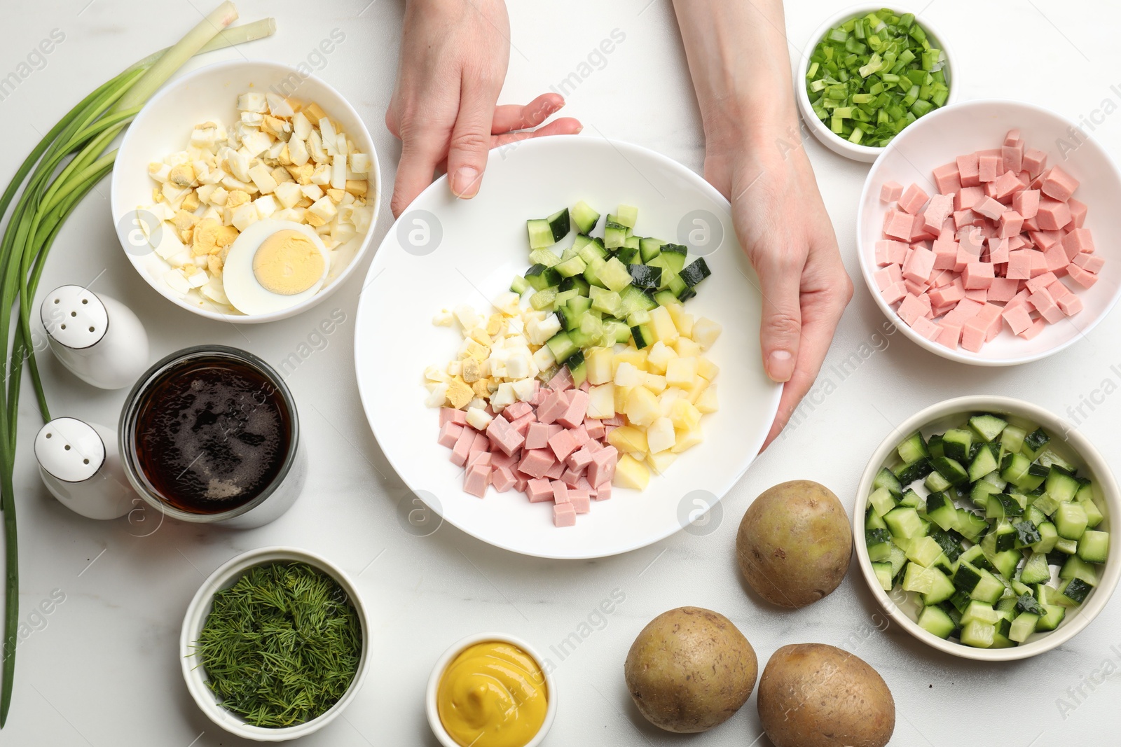 Photo of Making okroshka soup. Woman with bowl and different ingredients at white marble table, top view