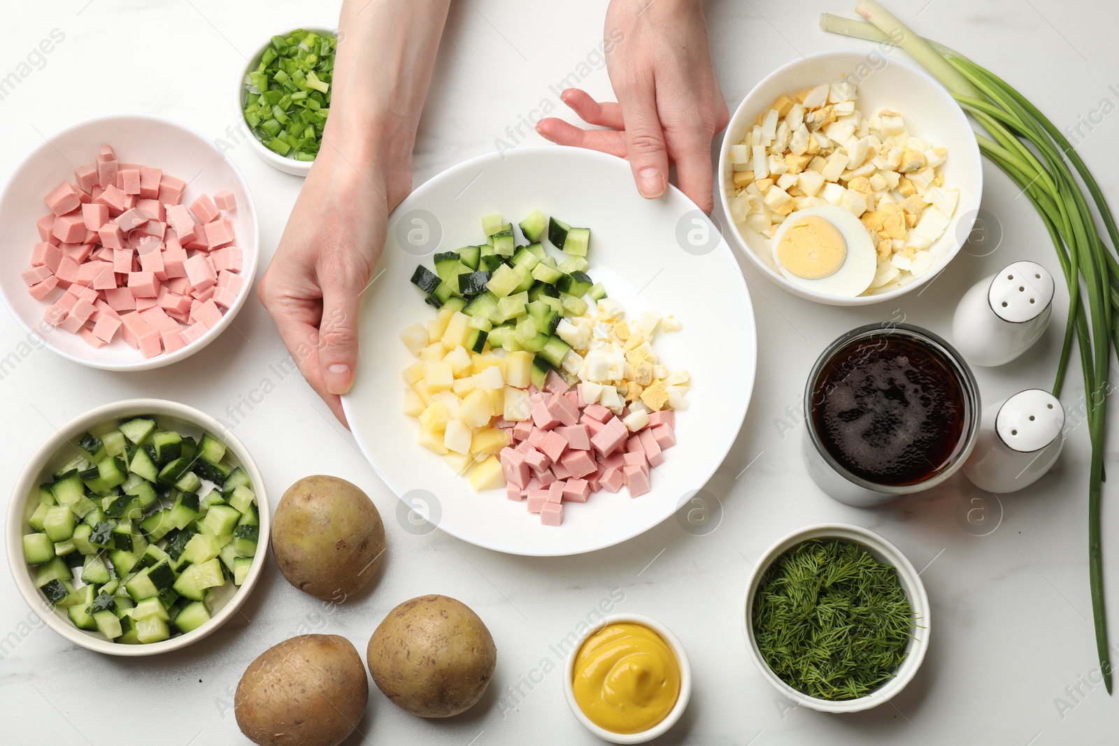 Photo of Making okroshka soup. Woman with bowl and different ingredients at white marble table, top view