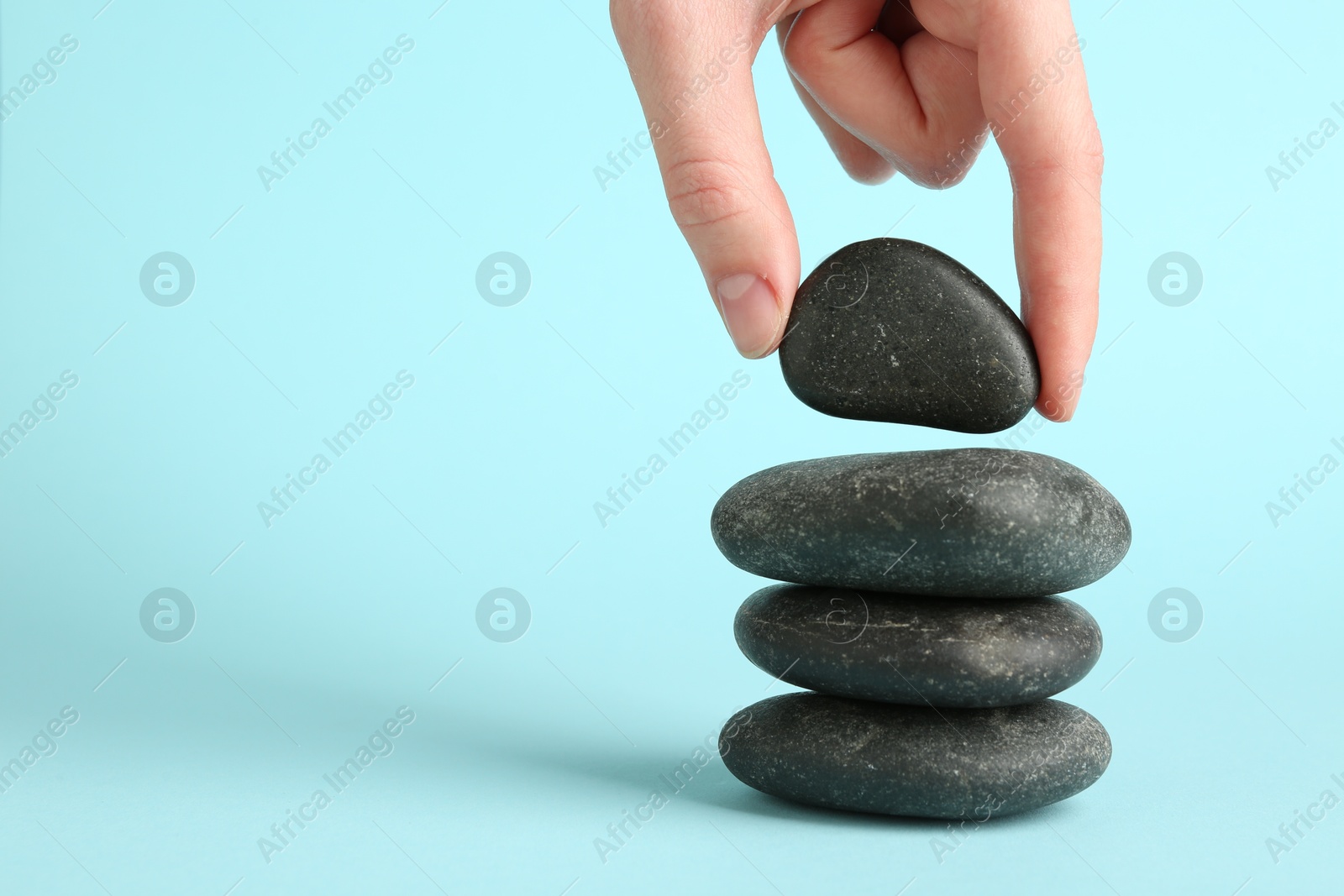 Photo of Woman making stack of stones on light blue background, closeup with space for text. Harmony and life balance