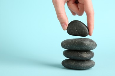 Photo of Woman making stack of stones on light blue background, closeup with space for text. Harmony and life balance