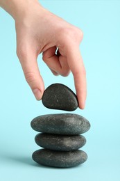 Photo of Woman making stack of stones on light blue background, closeup. Harmony and life balance