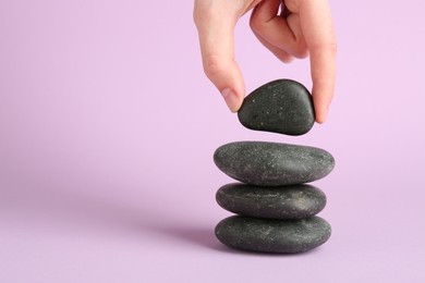 Photo of Woman making stack of stones on lilac background, closeup with space for text. Harmony and life balance