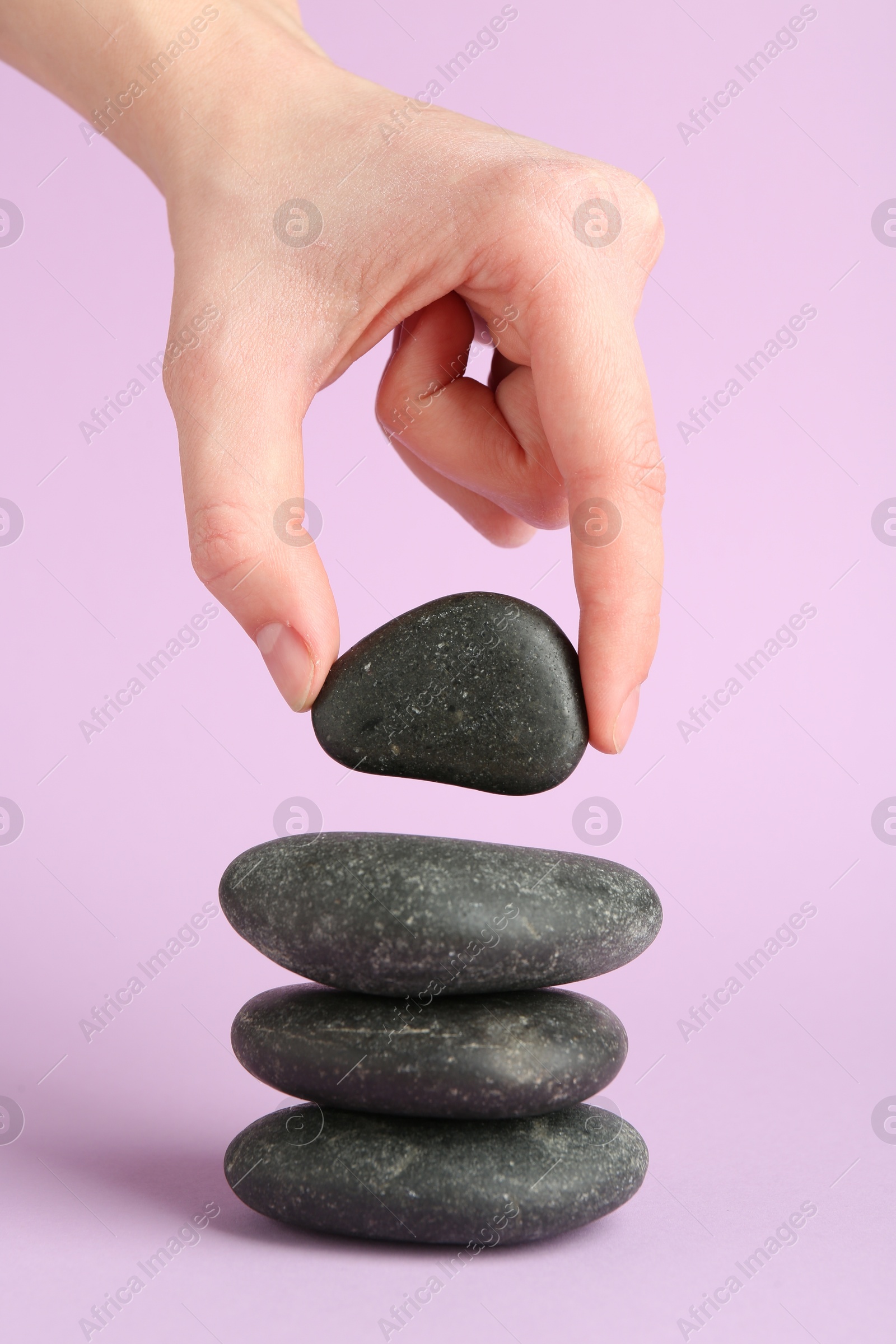 Photo of Woman making stack of stones on lilac background, closeup. Harmony and life balance