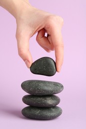 Photo of Woman making stack of stones on lilac background, closeup. Harmony and life balance